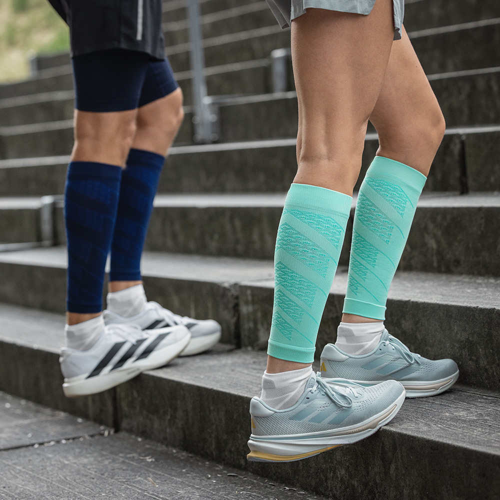 Treppentraining mit Kompressions-Sleeves in Mint und Navy Zwei Läufer beim Treppentraining im Freien. Sie tragen Run Performance Sleeves mit Kompression in Mint und Navy, die die Waden stabilisieren und die Durchblutung fördern.