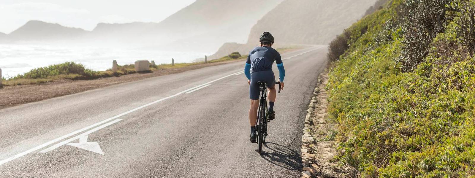 Cycliste avec manches sur route côtière Cycliste portant des manches bleues et roulant sur une route en pente avec vue sur la mer