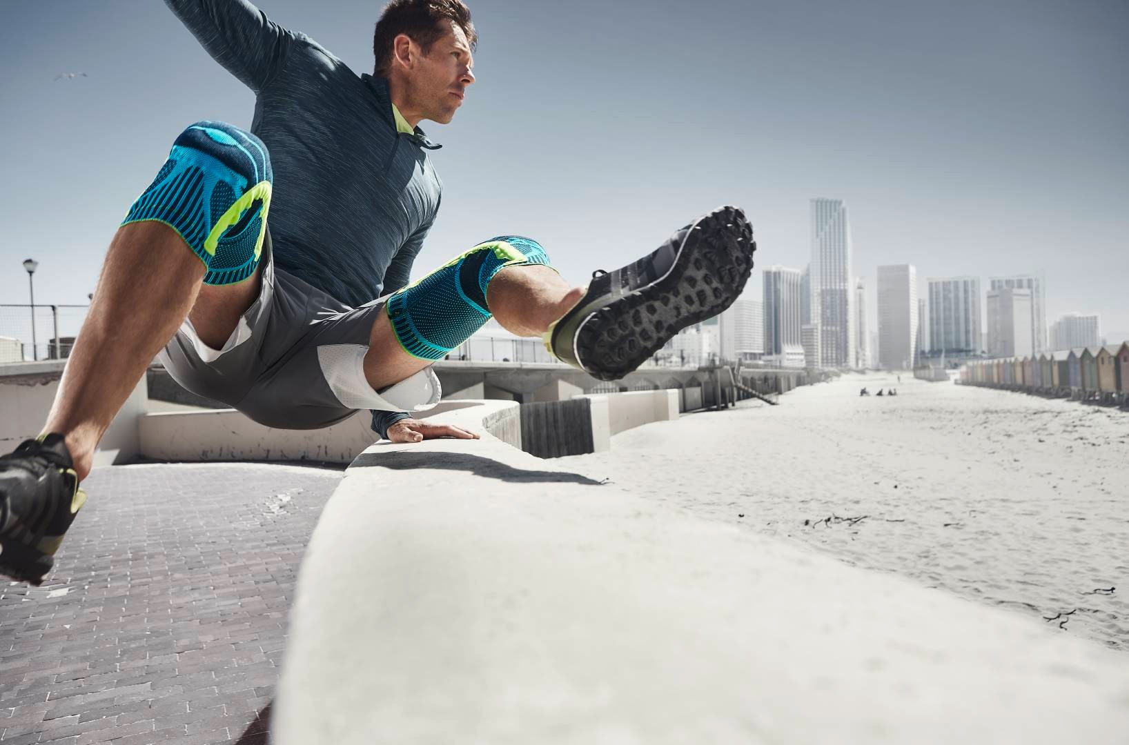 Homme avec deux genouillères saute au cours de l'Urban Running par-dessus un obstacle, en arrière-plan des gratte-ciels