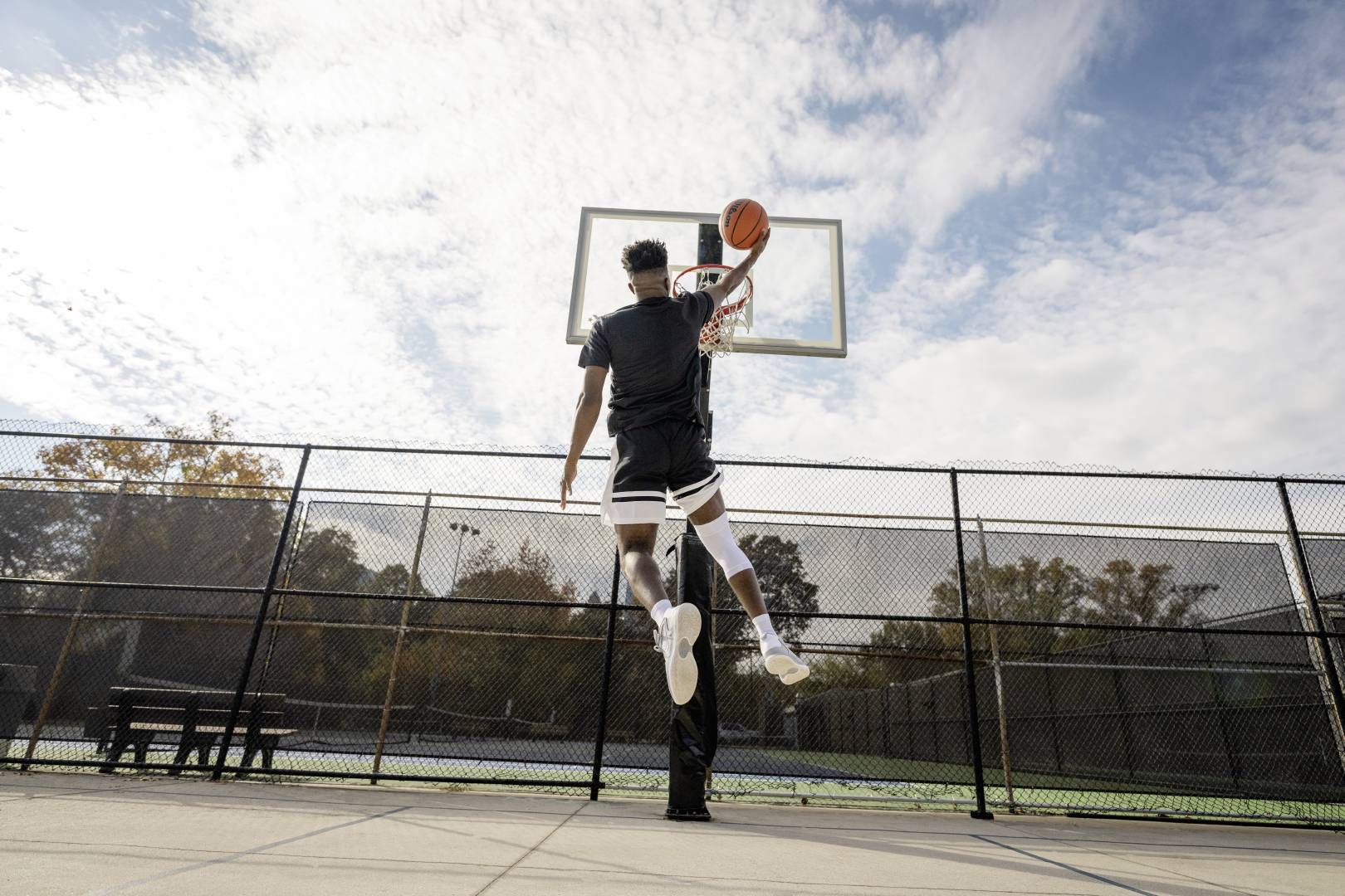 Basketballspieler springt zum Dunking Basketballer mit weißer Kniebandage beim Dunking auf einem Streetballfeld