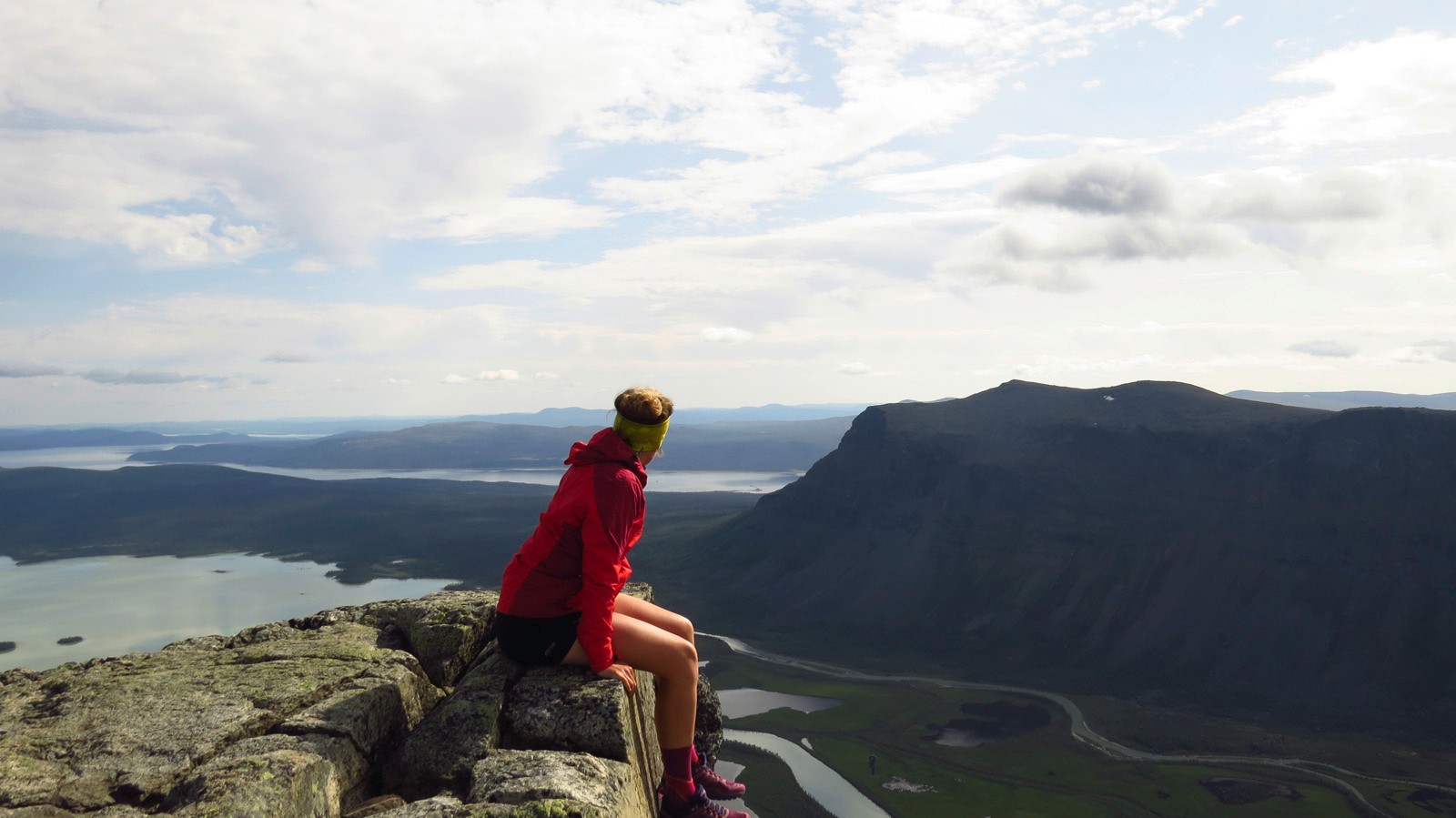 Femme assise sur un promontoire rocheux regardant au loin vers les montagnes et les lacs