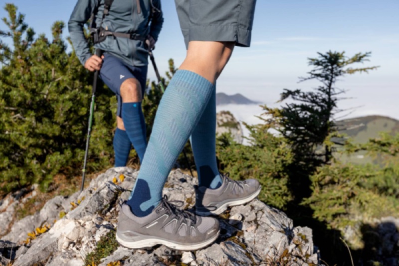 Wandersocken Outdoor Performance Compression Socks grün Frau mit grünen Wandersocken tritt auf einen Felsen in der Dämmerung