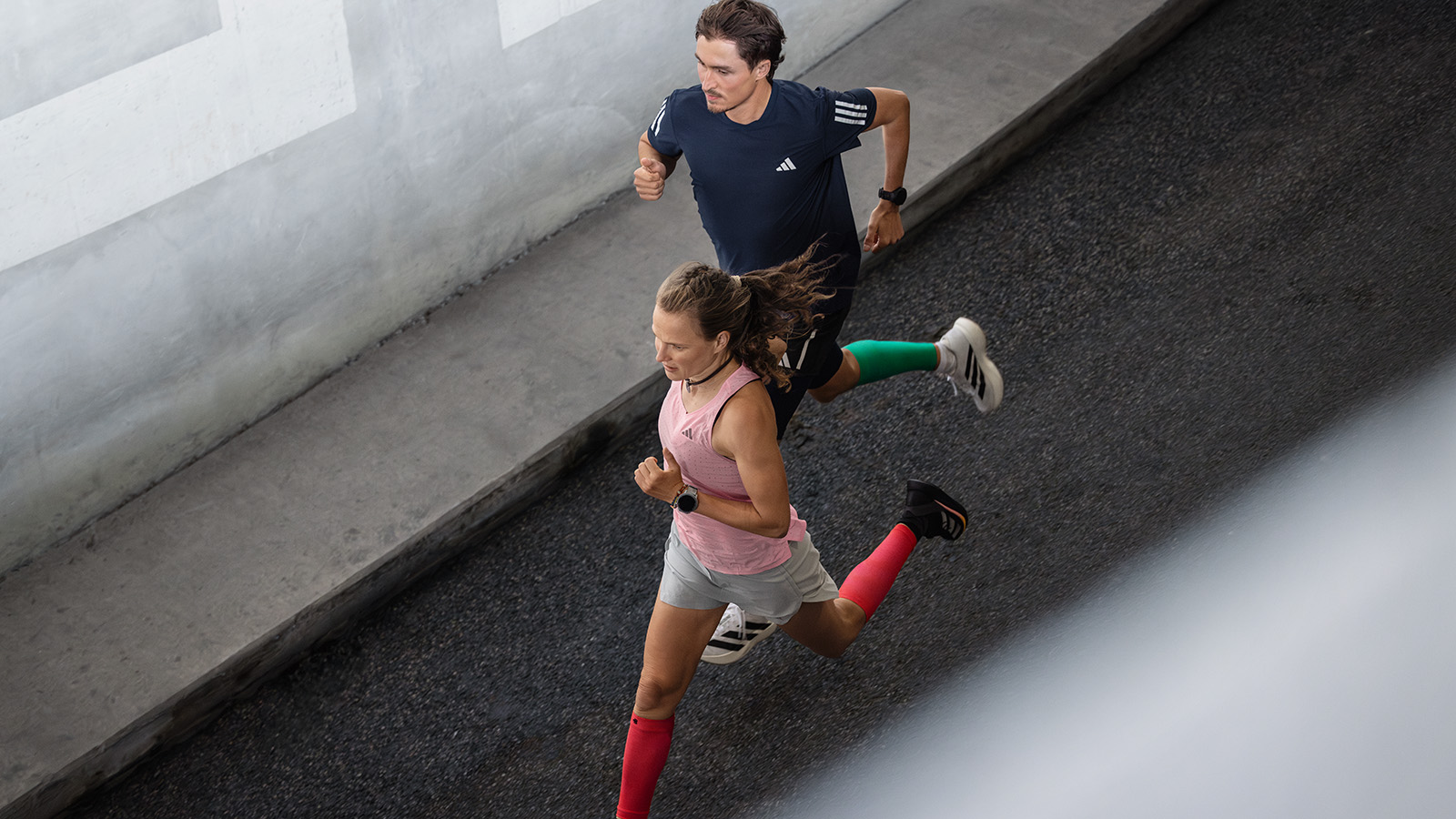 Marathon-Trainingsplan : la course longue et détendue devrait toujours constituer la base de ton entraînement Deux coureuses courent à côté d'un mur au design moderne dans un environnement urbain et discutent