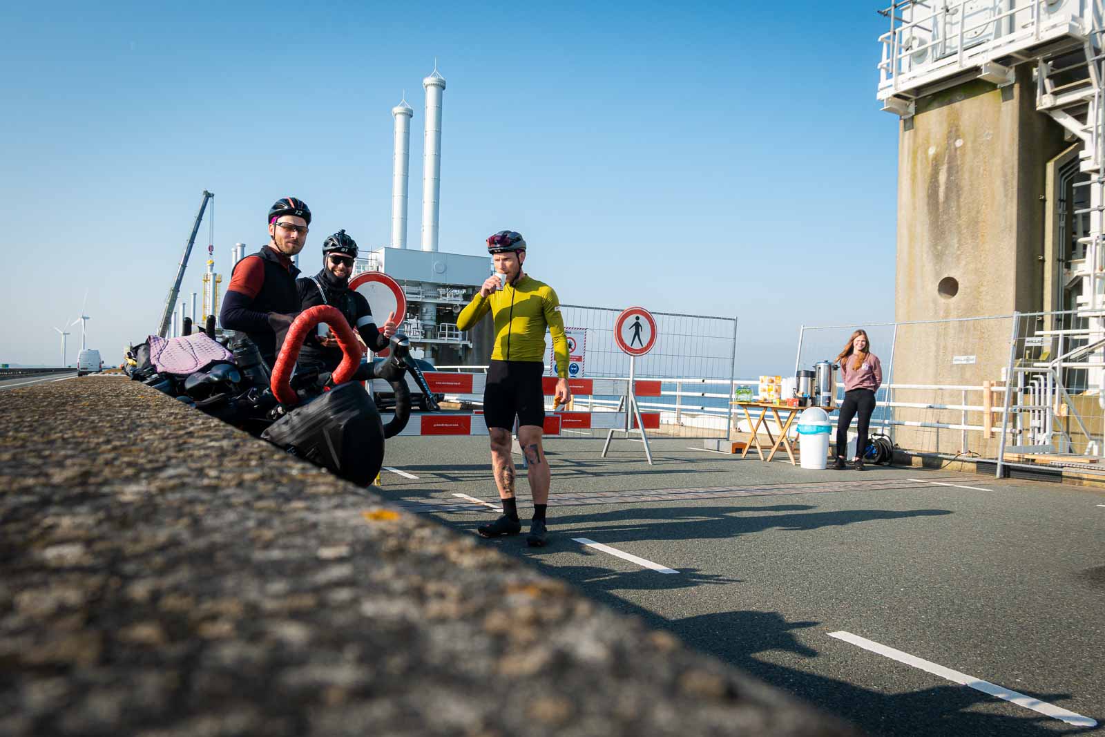 Radfahrer warten an einer Baustelle und trinken Kaffee An einer Brückenbaustelle stehen drei Radfahrer und warten, dabei trinken sie Kaffee und essen Kekse