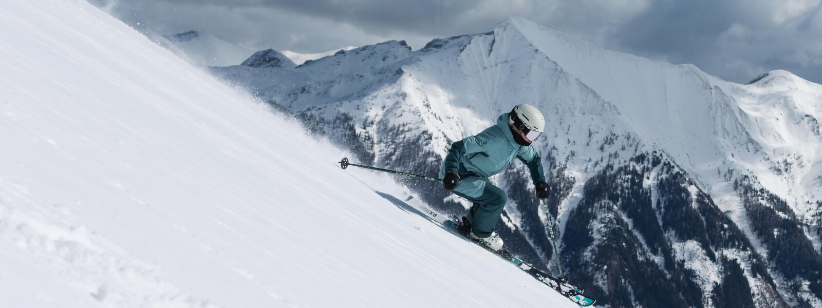 Skifahren: Ausgestattet mit Bauerfeind Produkten Skifahrer fährt eine Poste herunter, im Hintergrund befinden sich Schneebedeckte Berge