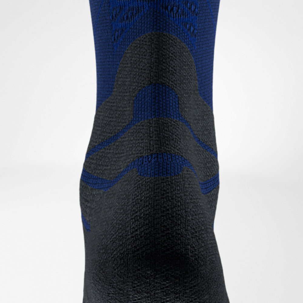 Blauer Support, Schritt für Schritt. Detailaufnahme einer blau-schwarzen Laufsocke von Bauerfeind Sports, Rückansicht auf Höhe der Achillessehne. Das markante Polster schützt die Sehne vor Reibung im Schuh.