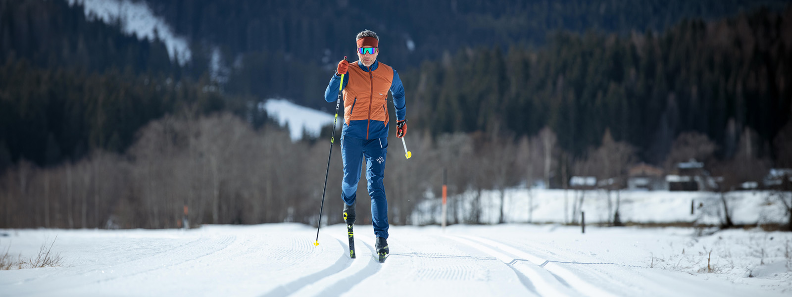 Abenteuer Langlauf: Mann unterwegs im Winterwald Ein Mann, frontal von der Ferne aus fotografiert, macht Langlauf. Im Hintergrund sind grüne Bäume des Waldes zu sehen