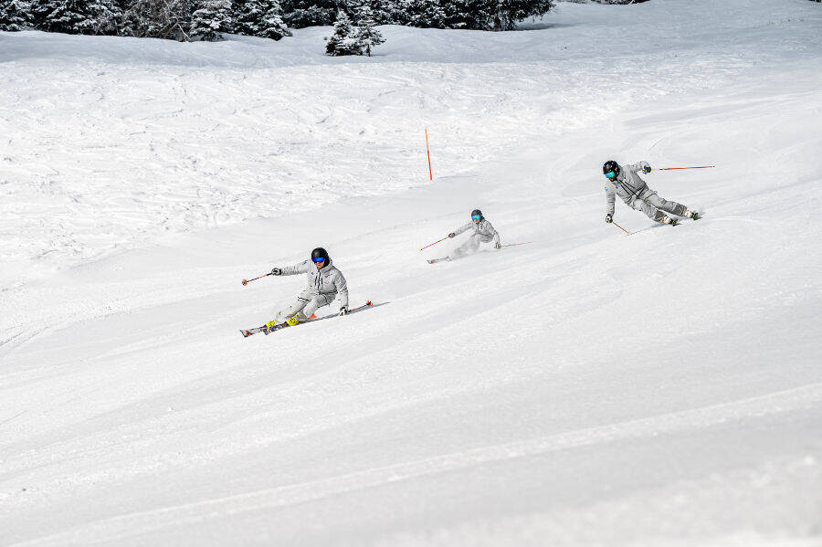 Trois d'un coup: Pars simplement en vacances d'hiver avec tes amis Trois skieurs vêtus de gris descendant ensemble en décalé et en positions inclinées