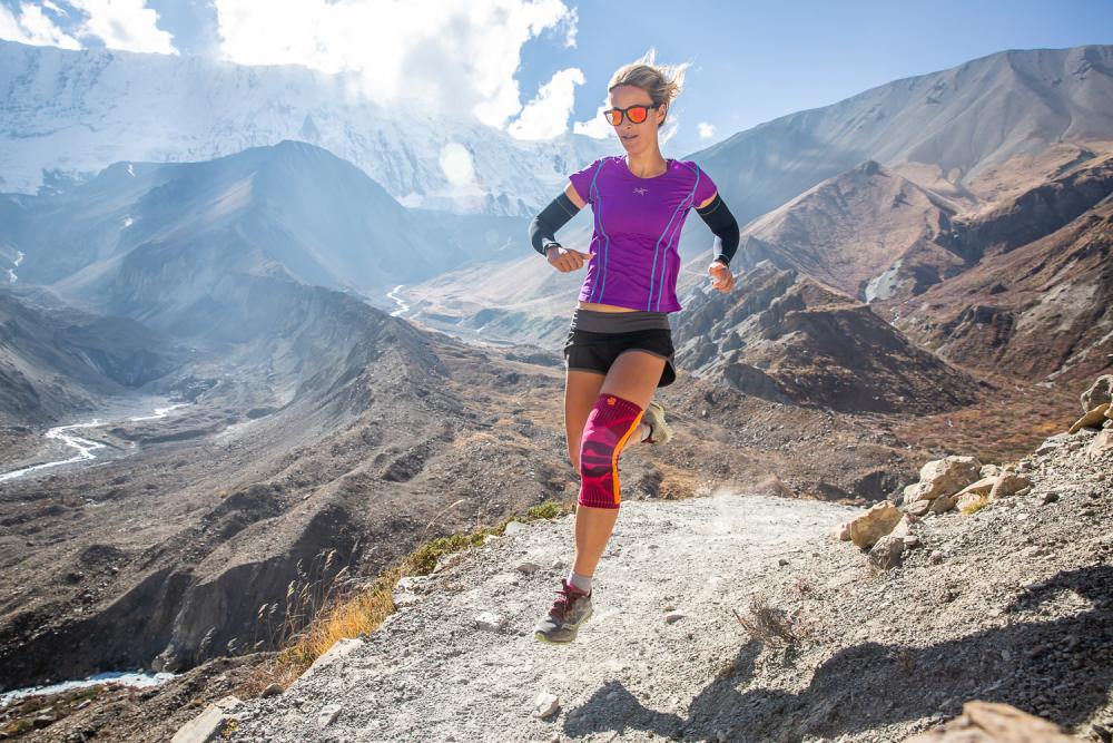 Trekking in Nepal - Hailey van Dyk mit der Sports Knee Support Frau läuft durch Hochgebirgslandschaft und trägt eine pinke Kniebandage