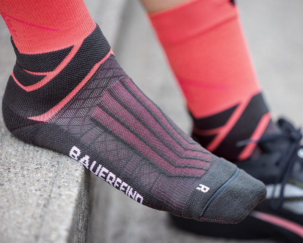 Mann mit blau-grauen Laufsocken sitzt auf einem Zaun und hat die Schuhe ausgezogen