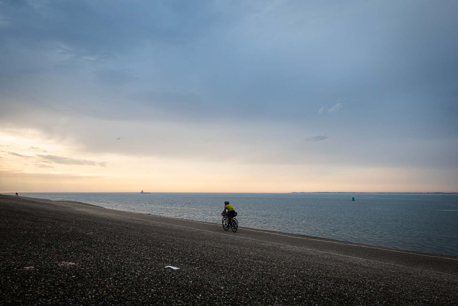 Radfahrer am Meer fahren dem Sonnenuntergang entgegen Zwei Teilnehmer des Race around the Netherlands fahren mit ihren Rädern der Abendsonne entgegen.