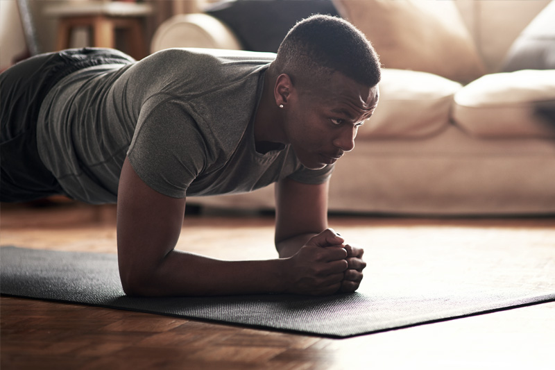 Entraînement de force pour les coureurs : La planche comme exercice de salon devant la télévision Homme faisant une planche dans le salon, en arrière-plan un canapé clair