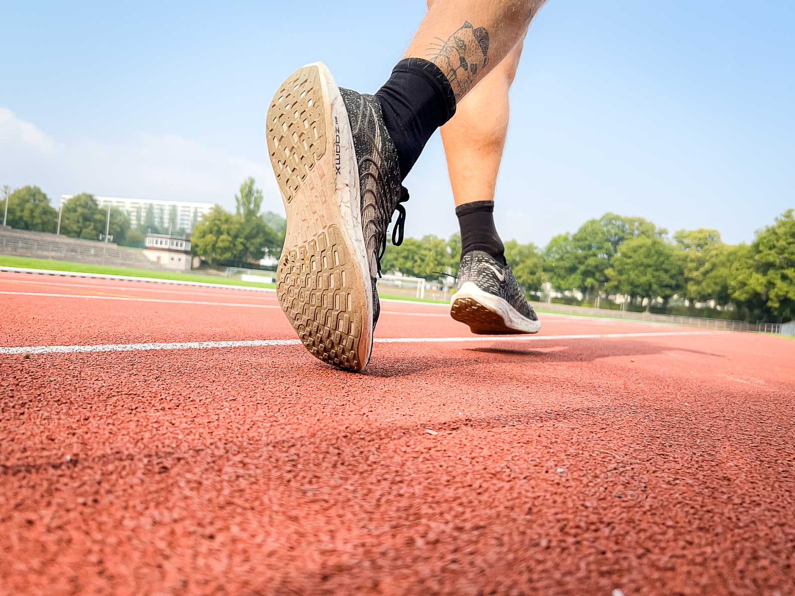 Lauftraining auf der Laufbahn – Fokus auf Entschlossenheit und Zielstrebigkeit. Nahaufnahme der Schuhe eines Läufers auf der roten Laufbahn, während er für das Training bereit ist. Die Szene symbolisiert Entschlossenheit und sportliche Zielstrebigkeit.