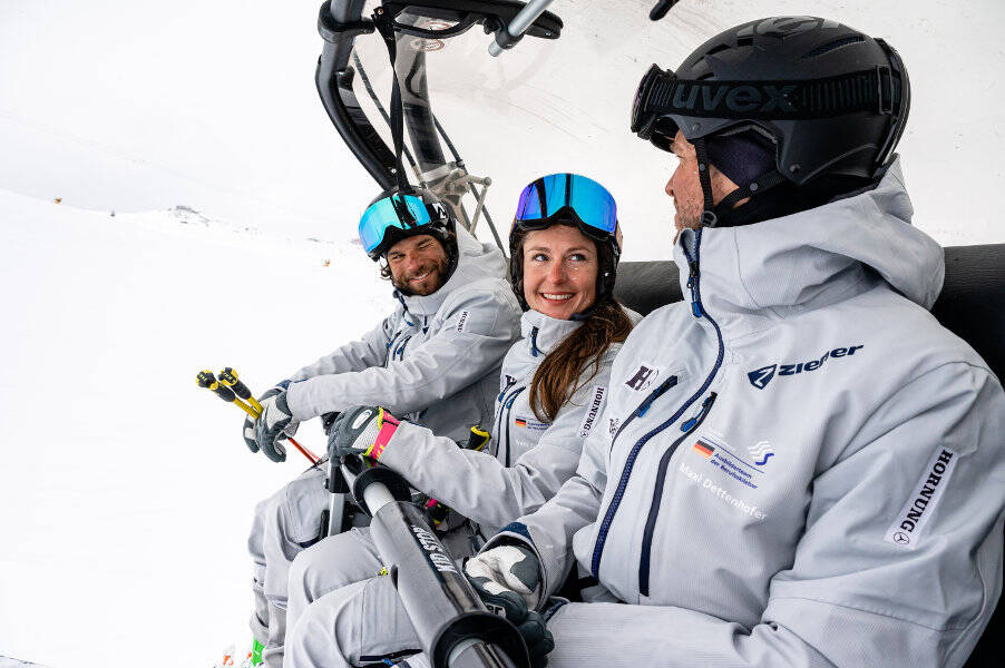 Pour encore plus de conversations amicales dans le télésiège Une femme et deux hommes en combinaisons de ski grises sont assis ensemble sur un télésiège, la femme regarde ses collègues en souriant