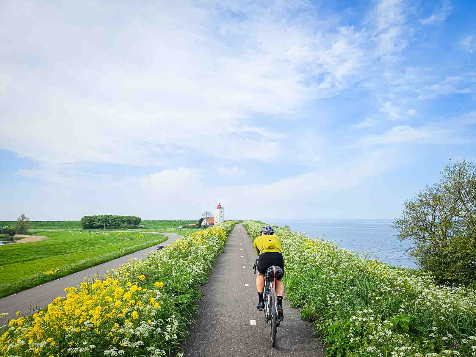 Cycliste sur une belle piste cyclable à côté de la mer, devant lui un phare Un cycliste roule sur une belle piste cyclable à côté de la mer, en direction d'un phare