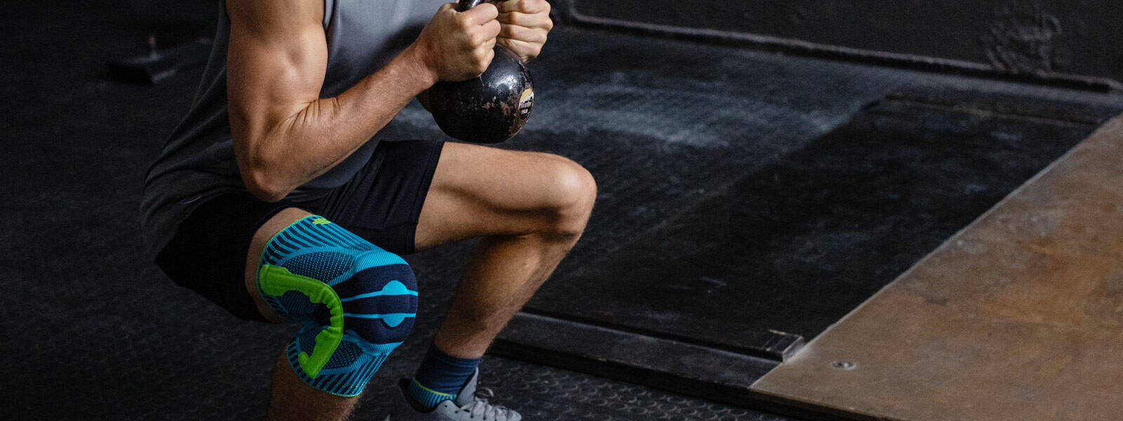 La Sports Knee Support te rend de grands services, surtout lors de l'entraînement de fitness Homme avec un bandage au genou fait une position accroupie profonde avec une kettlebell entre les deux mains