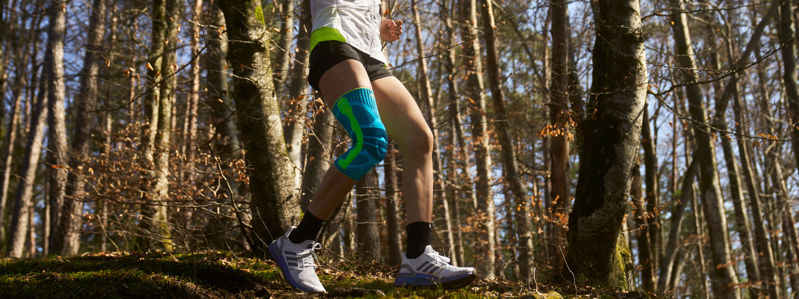 Réduction de la douleur grâce au Sports Knee Support lors de la course sur un terrain accidenté Anna Hahner court sur le chemin forestier avec une genouillère