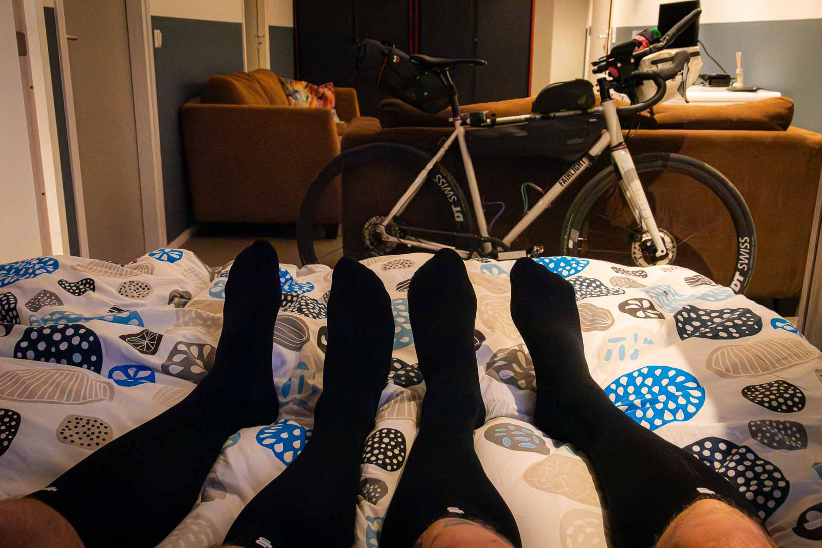 Deux cyclistes sont allongés dans leur lit et portent des chaussettes de récupération. Deux participants du Race around the Netherlands sont allongés dans leur lit après une journée éprouvante et portent des chaussettes de récupération.