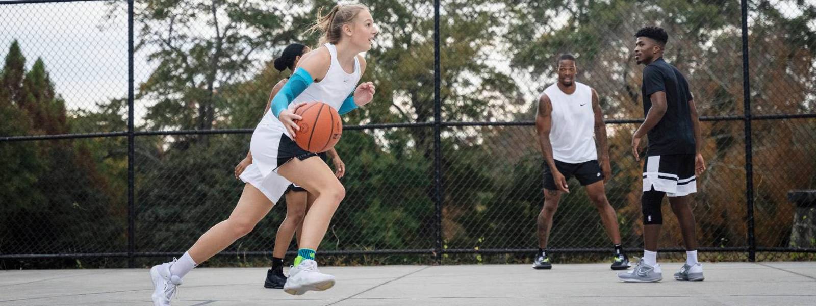 vier Basketballspieler im Spiel Basketball Spielerin dribbelt auf einem Freiplatz an ihren Gegenspielern vorbei und trägt dabei blaue Arm Sleeves
