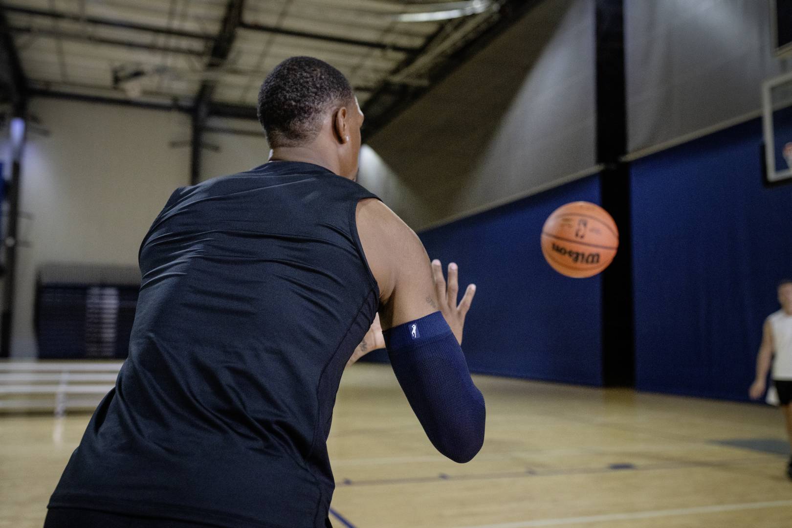 Joueur de basketball attrape le ballon et porte une manche Joueur de basketball avec une manche bleue en salle de sport attend un ballon qui lui est lancé par un autre joueur