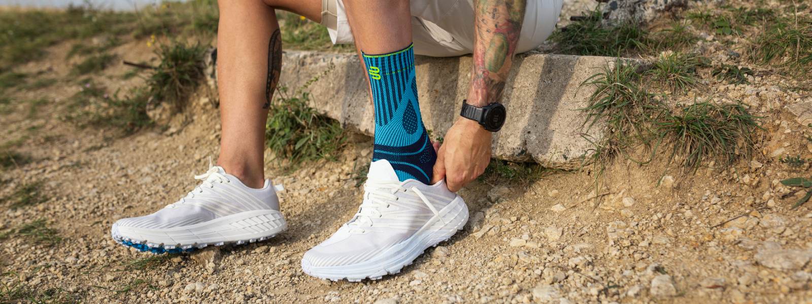 Courir encore plus en sécurité et sans douleur avec un bandage de tendon d'Achille Homme assis sur une pierre enfilant une chaussure de course par-dessus son bandage de tendon d'Achille