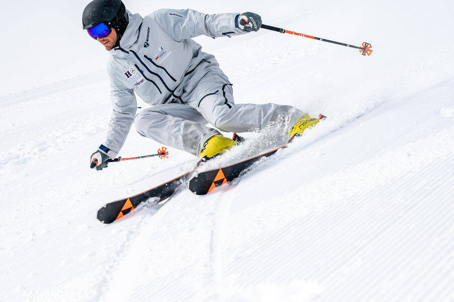 Sur une piste fraîchement préparée, la descente est toujours la plus amusante Skieur en costume gris légèrement incliné, devant lui on peut voir le motif strié de la piste préparée