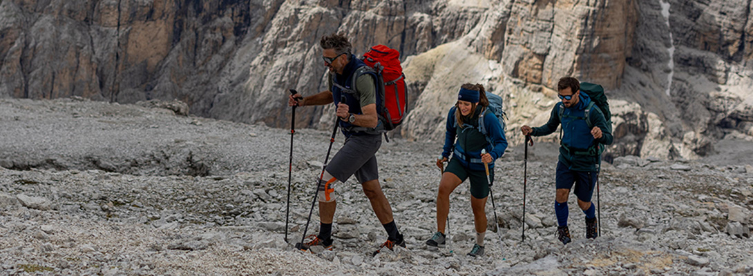 Wander Kniebandage beim Bergsteigen im Einsatz Drei Bergsteiger beim Wandern zwischen steinigem Geröll, der erste trägt eine Wander Kniebandage