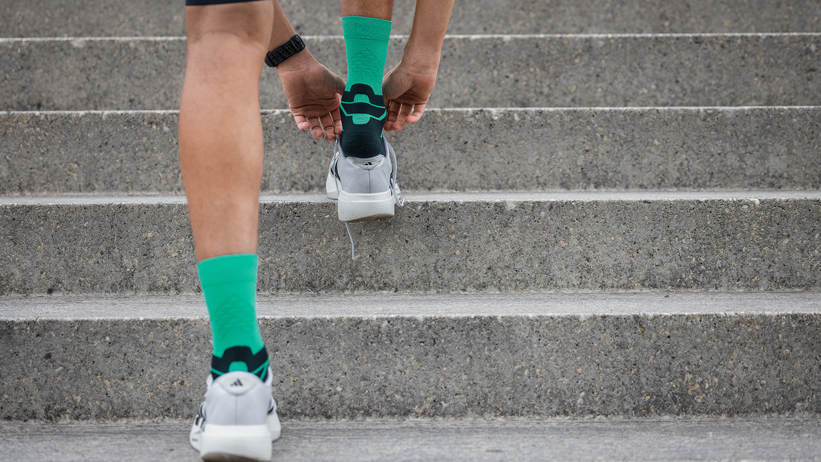 Mann mit blau-grauen Laufsocken sitzt auf einem Zaun und hat die Schuhe ausgezogen