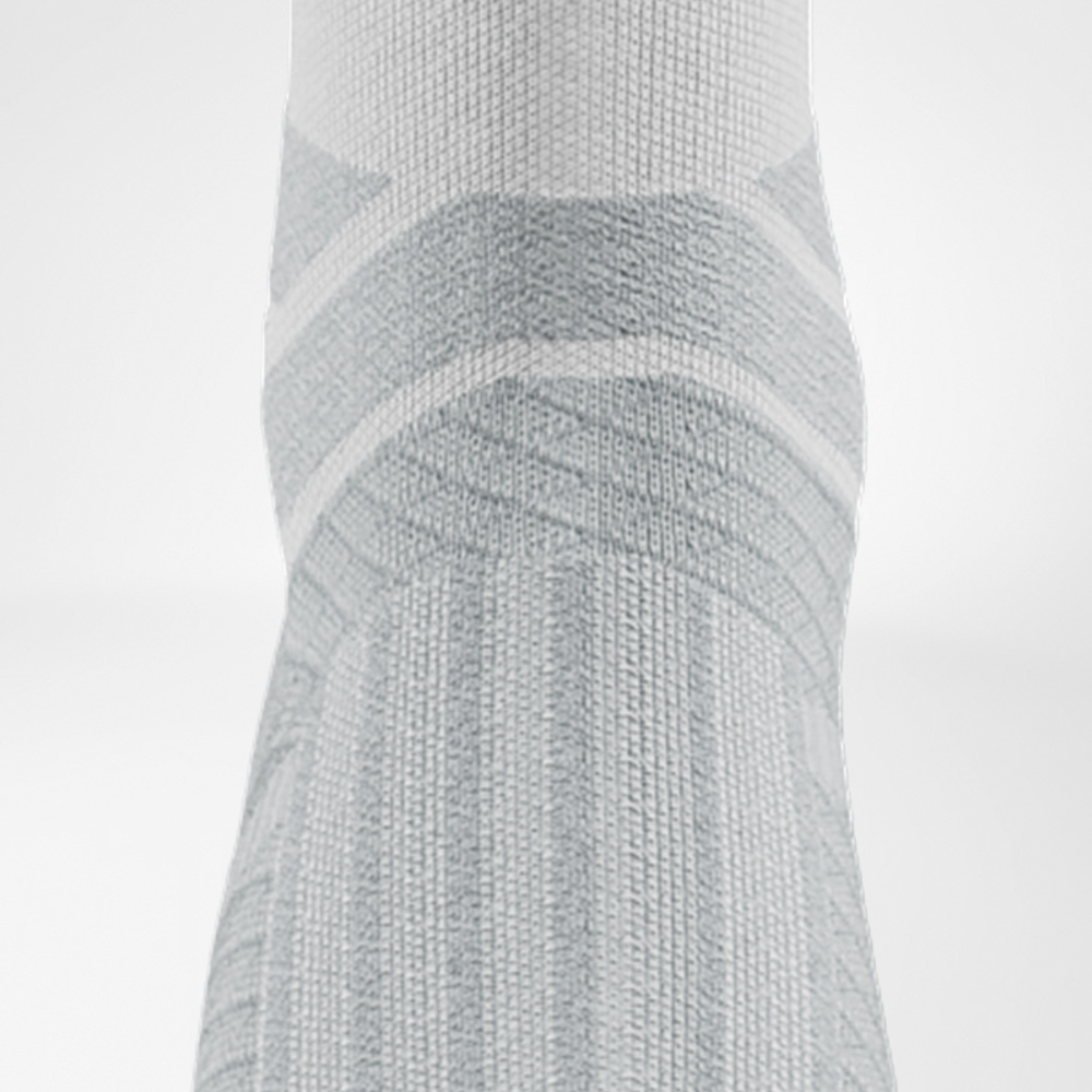 Unterstützende Zonen rund um das Sprunggelenk. Detailansicht des Sprunggelenks der weißen Run Performance Socks mit anatomischer Polsterung und Stützstrukturen.