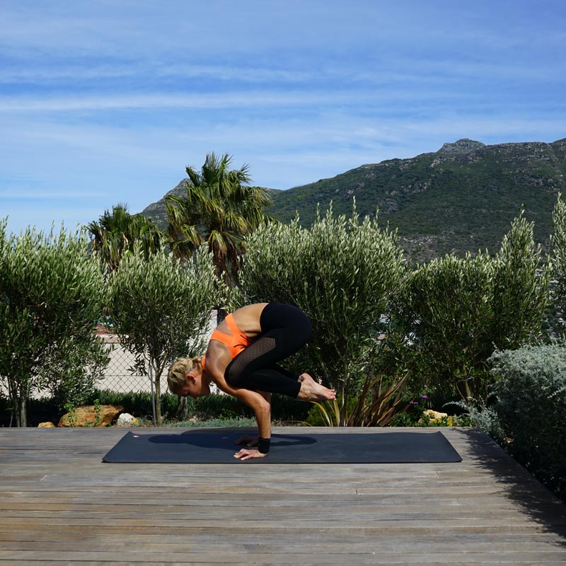 Yoga à la maison avec Sports Wrist Strap Femme faisant du yoga sur sa terrasse équilibre sur ses mains tandis que ses jambes sont suspendues derrière son torse en l'air