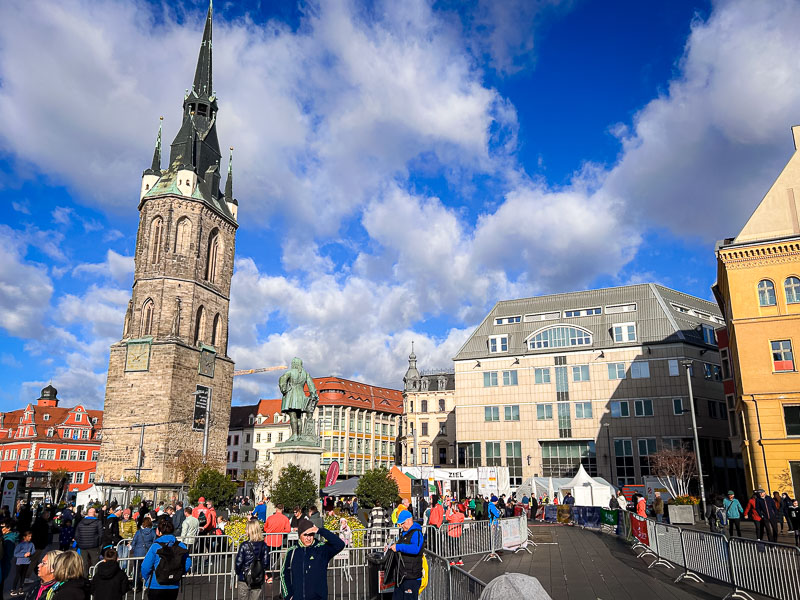 Der Marktplatz in Halle während des Mitteldeutschen Marathons mit dem Roten Turm im Hintergrund. Läufer und Zuschauer versammeln sich auf dem Marktplatz von Halle vor dem Start des Mitteldeutschen Marathons. Im Hintergrund steht der markante Rote Turm, eine Sehenswürdigkeit der Stadt.