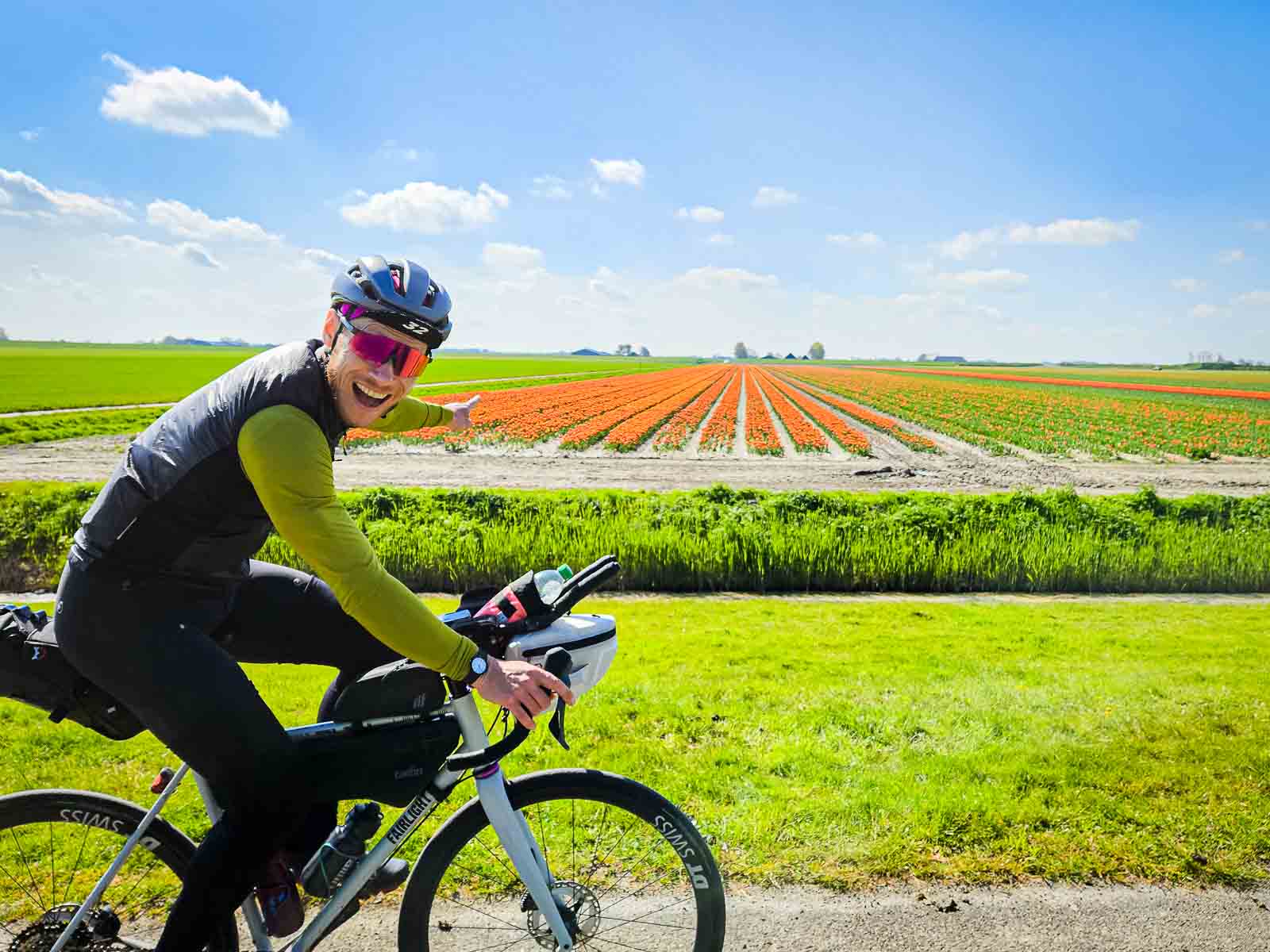 Cycliste rit en roulant vers la caméra et montre des fleurs colorées Un participant du Race around the Netherlands se réjouit à la vue de fleurs colorées et les montre du doigt