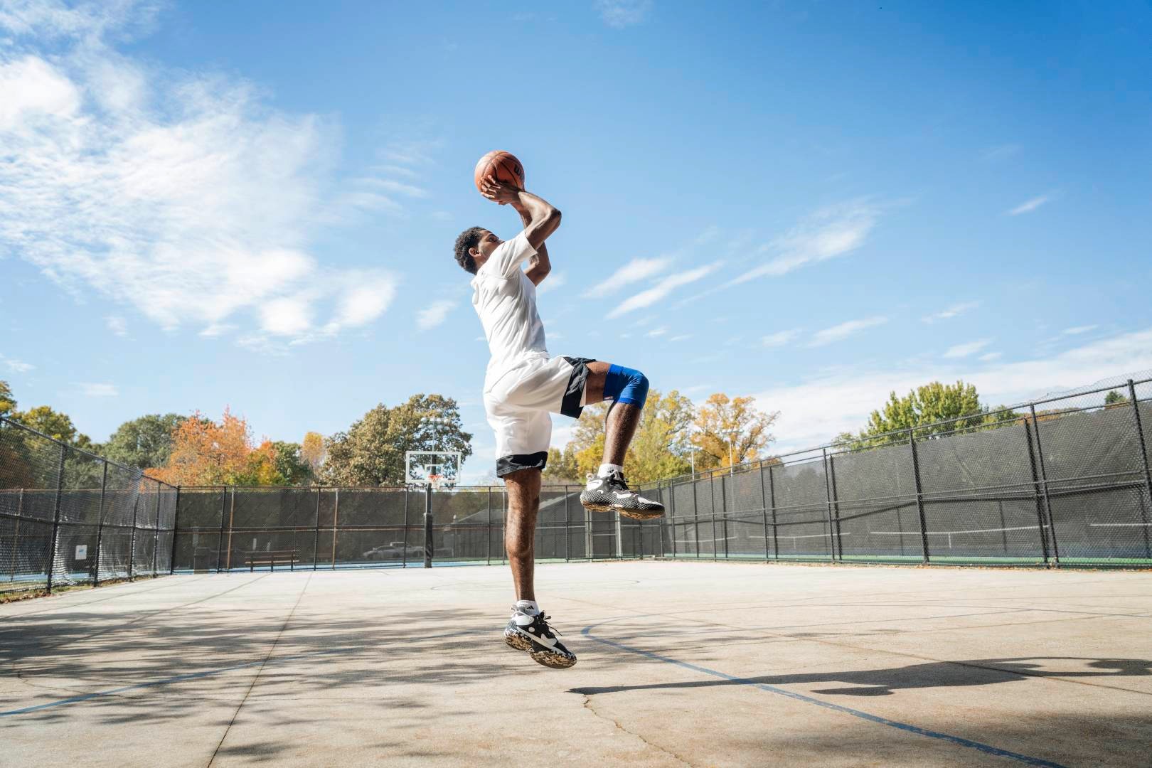 Le basketteur saute sur un terrain de rue pour le tir, les mains avec le ballon au-dessus de la tête, une jambe fléchie, l'autre pointant verticalement vers le bas