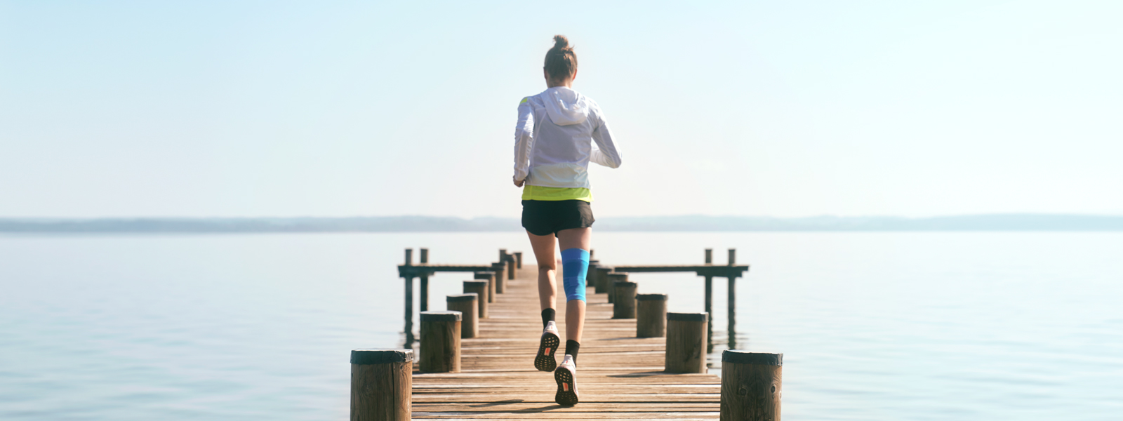 Sports Compression Knee Support pour éviter les douleurs arrière du genou en courant Anna Hahner court avec son Sports Compression Knee Support sur une passerelle en direction du lac