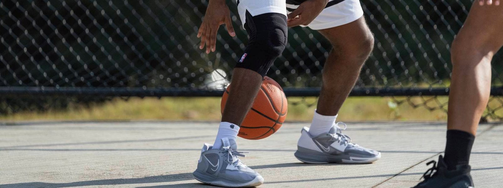 Knee Support NBA au basketball Joueur dribble sur un terrain de streetball avec un basketball et porte un Knee Support NBA noir