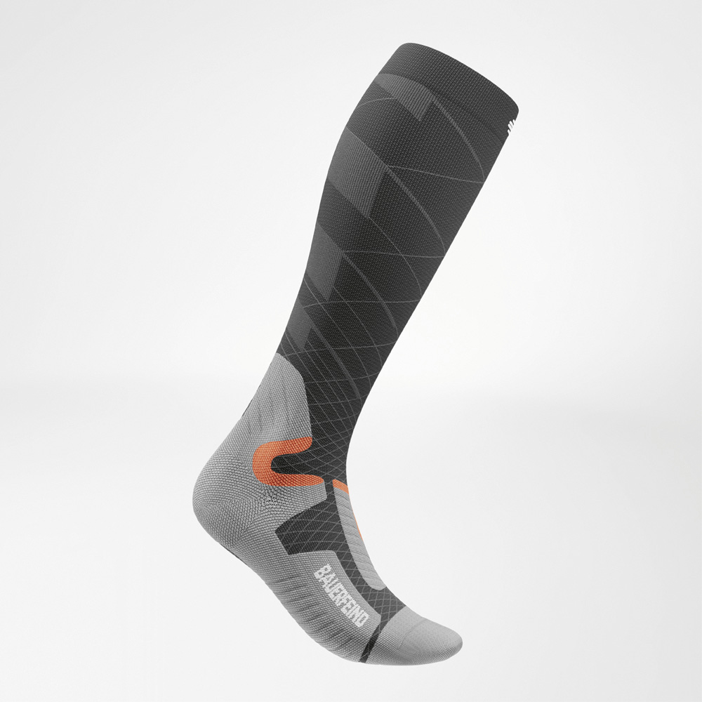 Seitliche Ansicht einer kniehohen Bauerfeind Sports Ski Performance Socke in Anthrazit, Grau und Orange. Die Kompressionssocke zeigt eine dynamische Linienstruktur und ist anatomisch an den Fuß angepasst.
