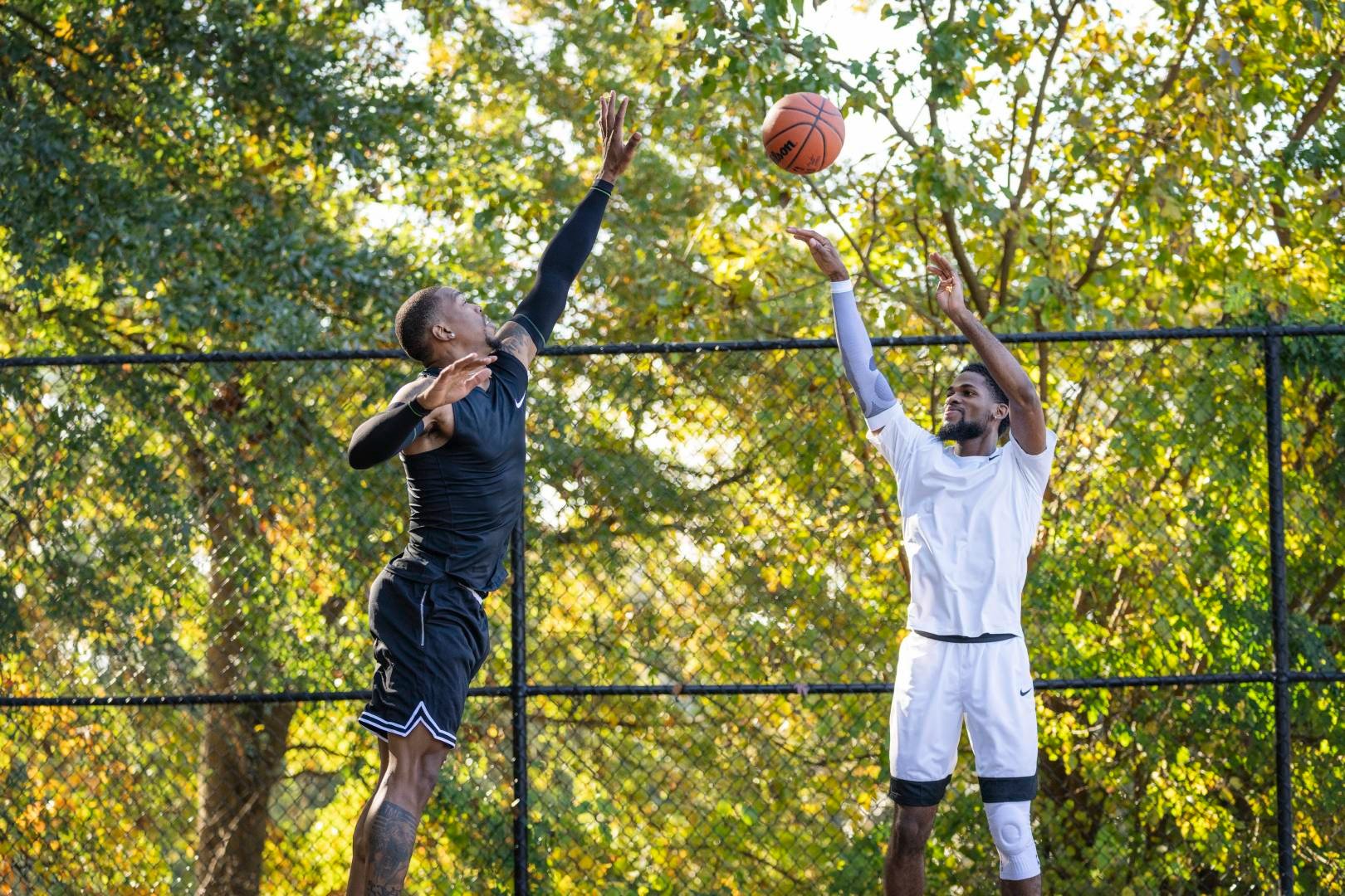 Joueur de basketball en tenue de jeu noire tente de bloquer le tir de son adversaire en tenue blanche haut au-dessus du sol