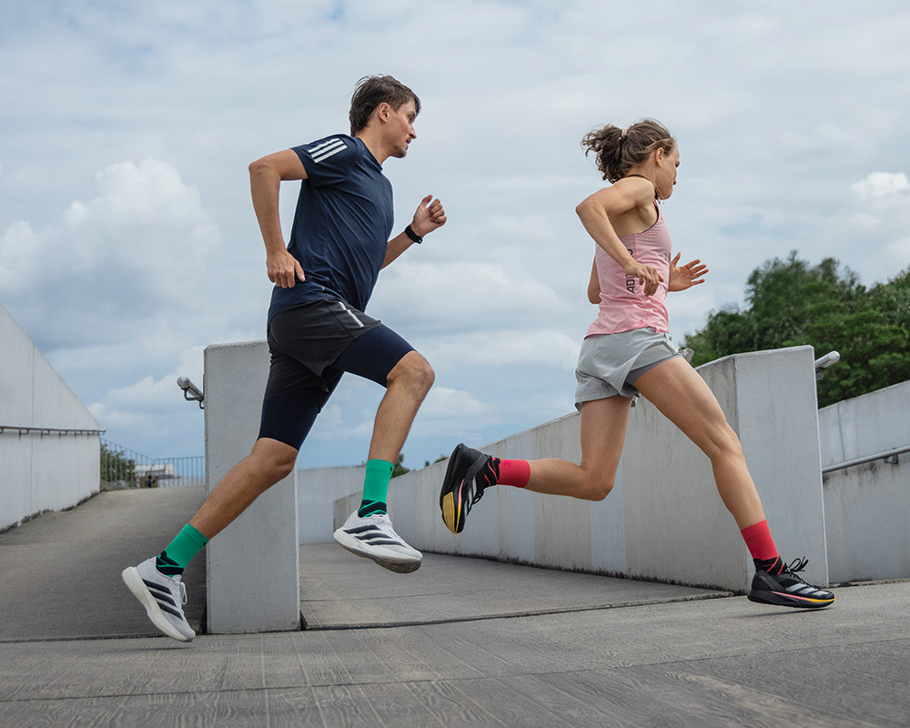 Esthétique synchronisée : Le design de nos Run Performance Socks convainc particulièrement en équipe Deux jambes fines de coureur avec des chaussettes de course blanches et roses montent des marches en pierre légèrement en décalé