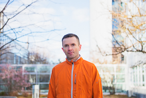 Ein Mann in orangener Jacke steht in einem Innenhof vor einem Gebäude