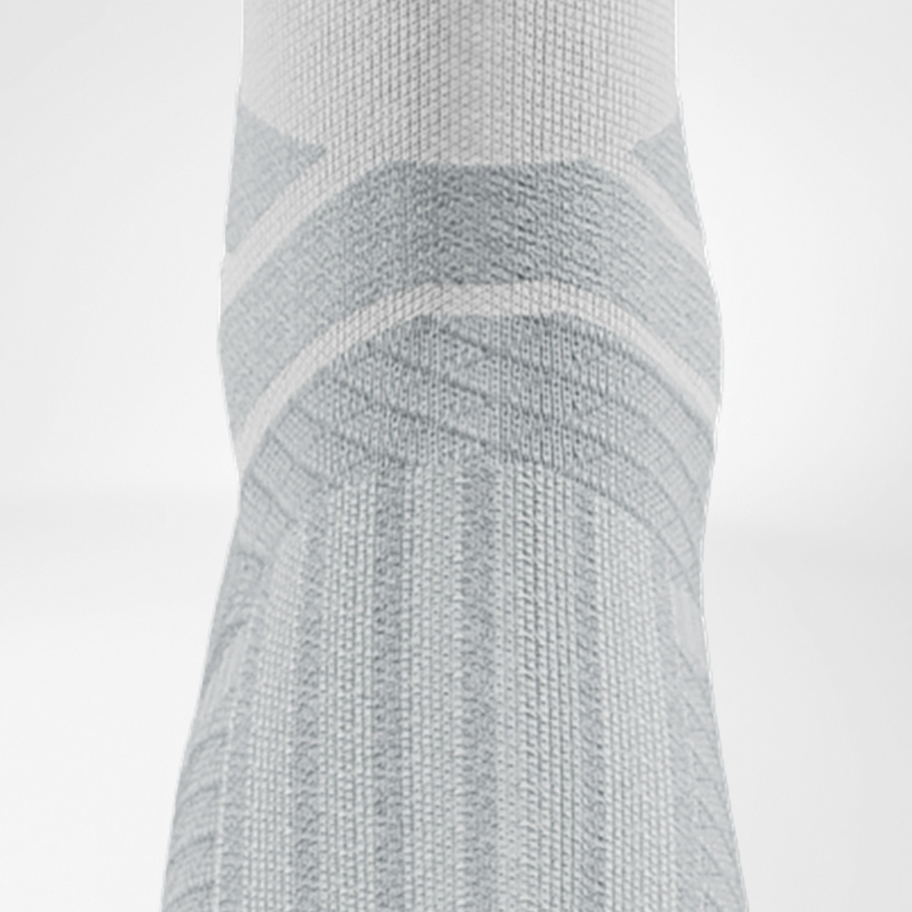 Weiß wie die Zielgerade im Morgengrauen. Rückansicht einer weißen Laufsocke mit hellgrauen Akzenten. Im Zentrum ist die Polsterung an der Achillessehne deutlich zu sehen.