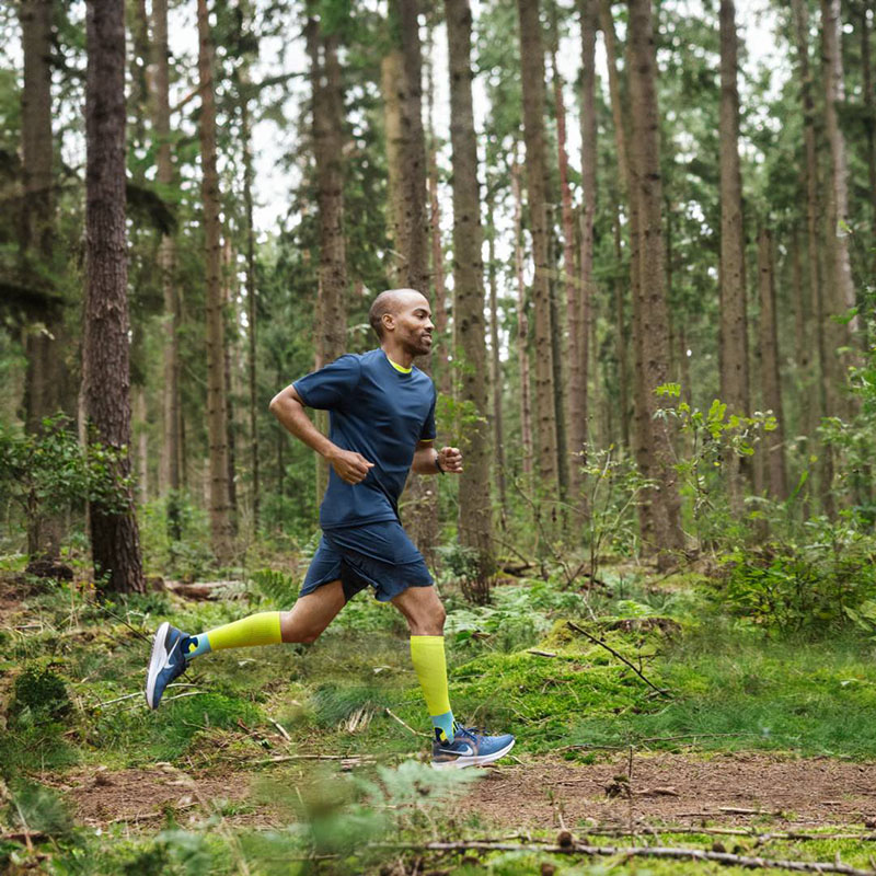 Coureur court à travers une forêt et porte des bas de compression Un coureur court rapidement à travers une forêt dense et porte des chaussettes de compression