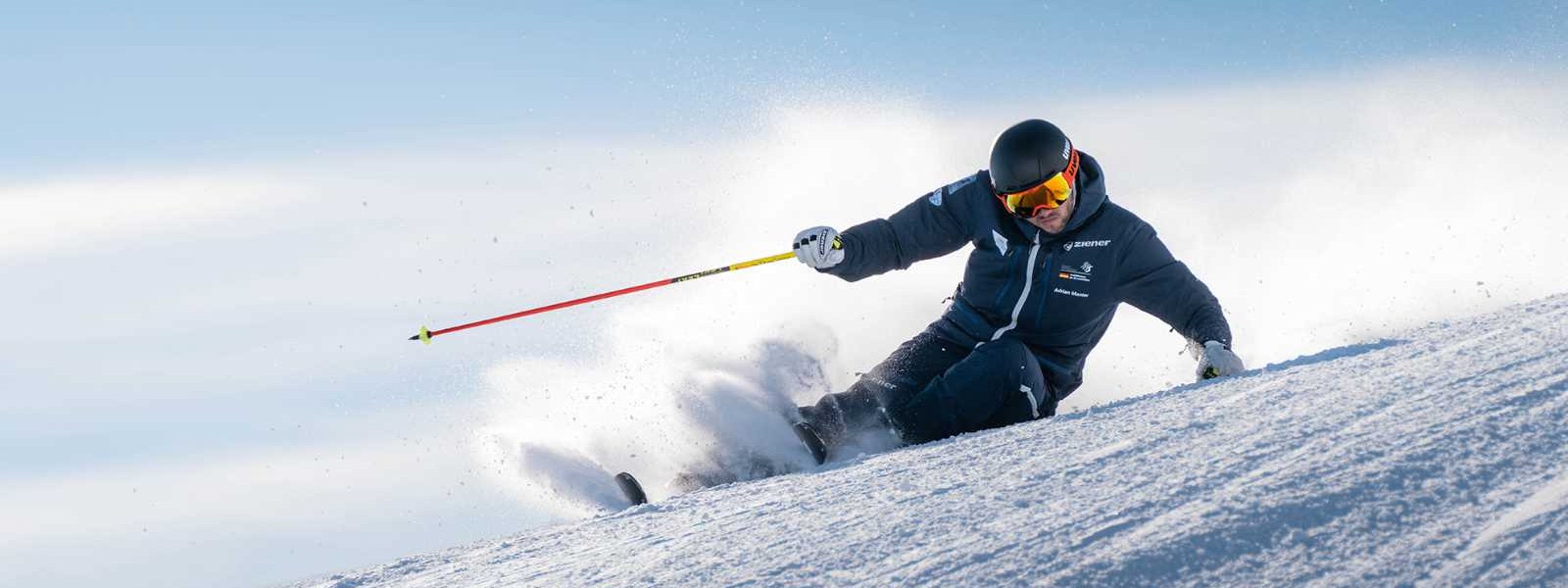 Born to ski: Teilst Du unsere Leidenschaft für Schnee und wunderschöne Abfahrten? Skifahrer in dunklem Anzug in extremer Schräglage bei der Abfahrt