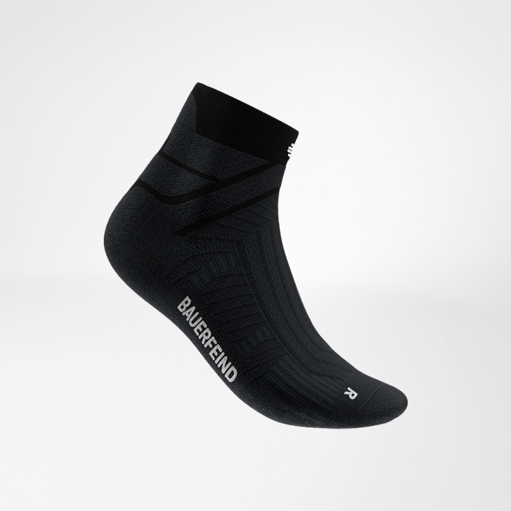 Dynamisch und kraftvoll – die schwarze Socke im Fokus. Schwarze Run Performance Low Cut Socke von Bauerfeind in seitlicher Ansicht, die den Spannbereich, das atmungsaktive Strickmuster und den seitlichen Bauerfeind-Schriftzug zeigt.