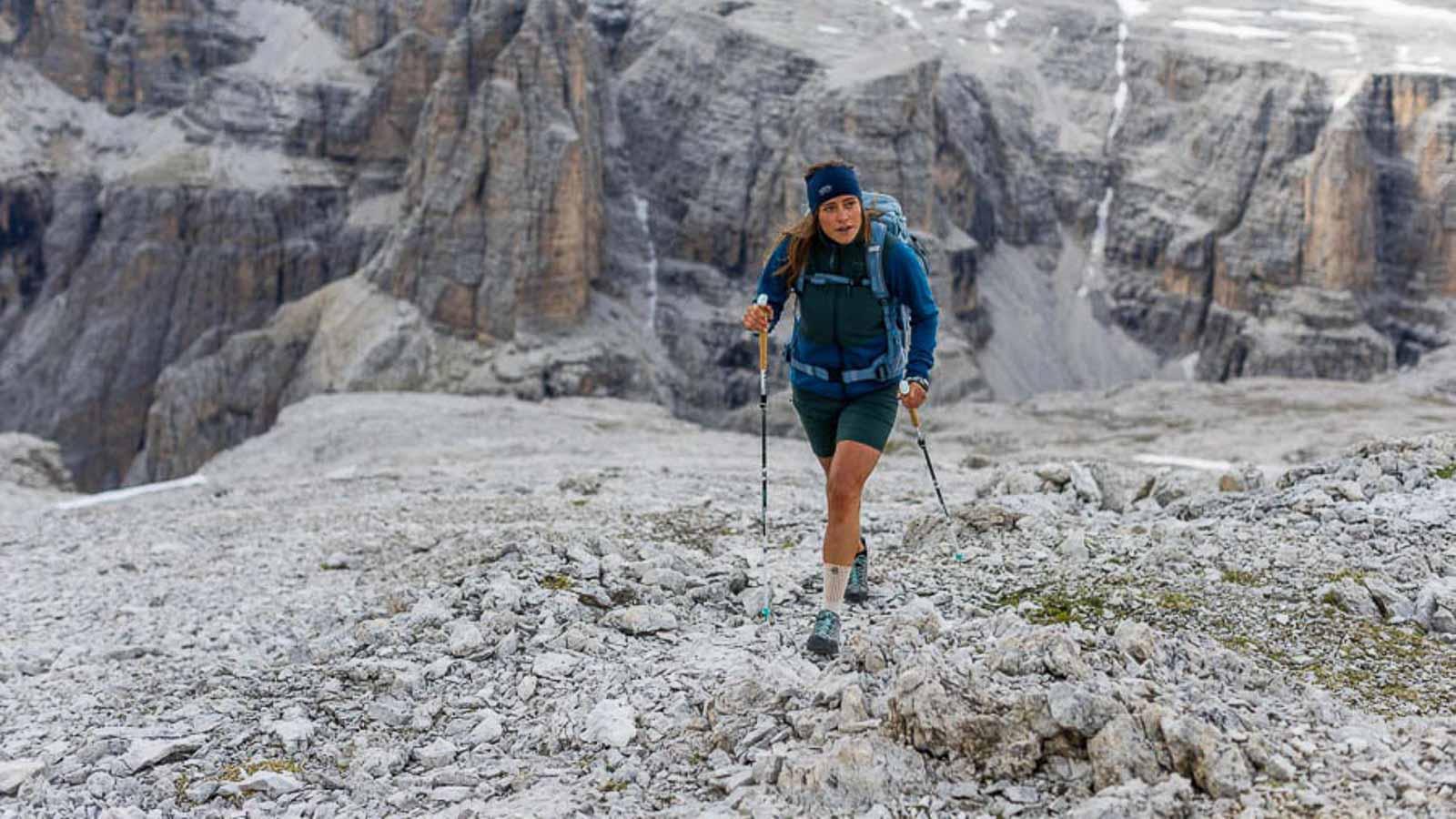 Une randonnée exigeante mais belle dans les Dolomites Une randonneuse dans les Dolomites marche avec des bâtons sur un éboulis et porte une bande de randonnée.