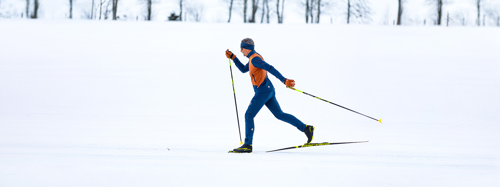 Farbenfroher Skilanglauf im Winterwunderland Ein Mann in orange-blauer Kleidung macht Langlauf durch den Schnee.