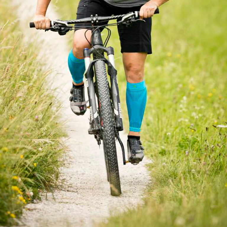 Vue frontale cycliste porte des manchons de mollet en roulant sur un chemin de gravier en VTT
