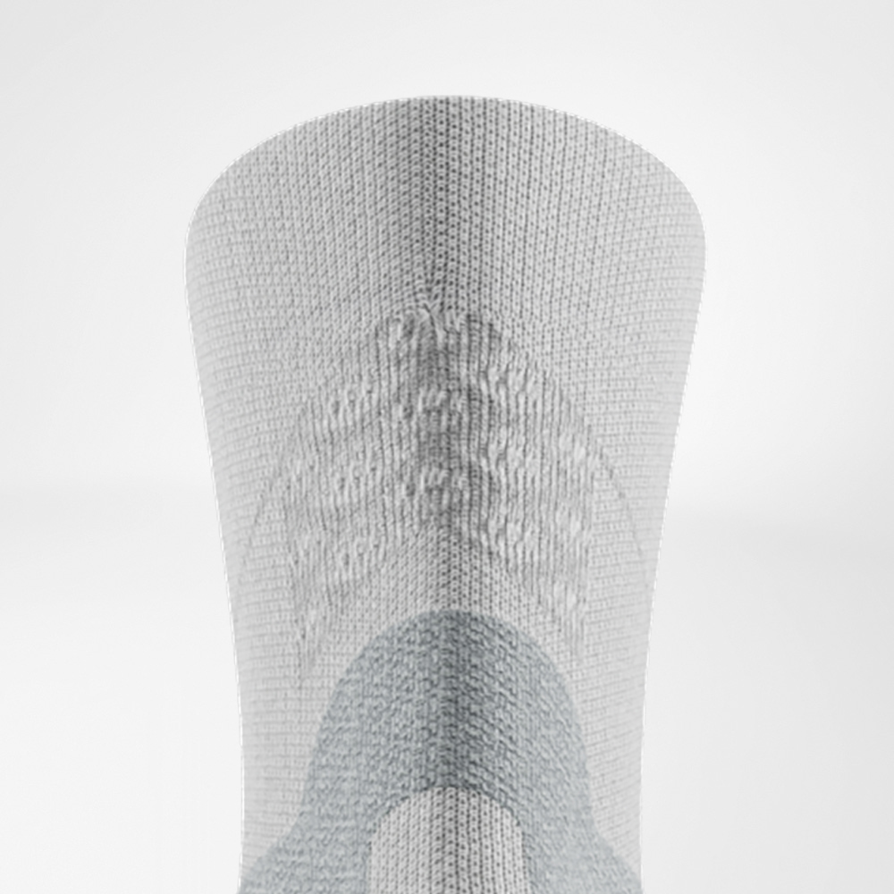 Leichtfüßig in Weiß – bereit für die nächste Runde. Nahaufnahme der Rückseite der weißen Run Performance Midcut Socke: graue Achillessehnen‑Komfortzone, gestrickte 3D‑Dots am Bündchen und stützende Strickzonen an der Wade.