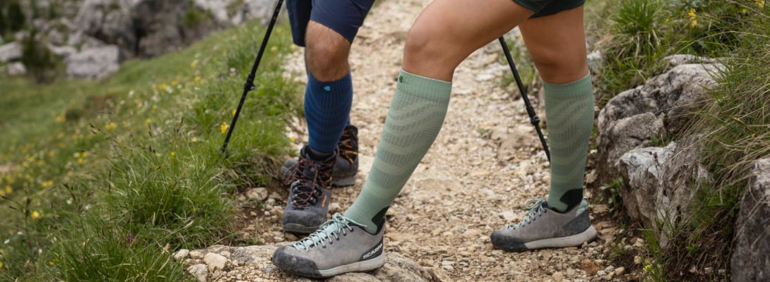Merino-Wandersocken blau beim Wandern Zwei Personen wandern über Felsen sie tragen Merino-Wandersocken im Hintergrund sind Bäume zu sehen