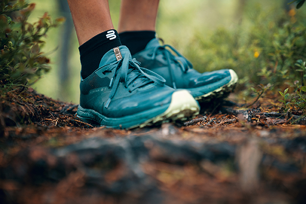 Passe Deine Schuhe unbedingt dem Untergrund an: Ein großes Profil brauchst Du häufig nur im Gebirge Nahaufnahme Grüne Wanderschuhe auf einem Waldboden