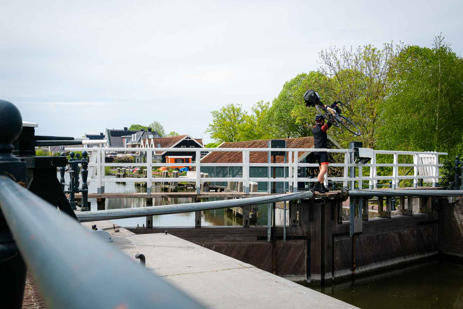 Radfahrer trägt sein Fahrrad über Schleuse Ein Radfahrer der beim Race around the Netherlands teilnimmt trägt sein Fahrrad über eine Schleuse.